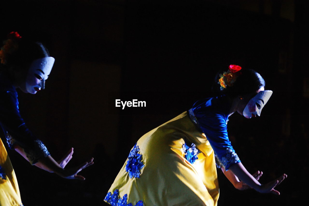 Side view of women with mask dancing on stage