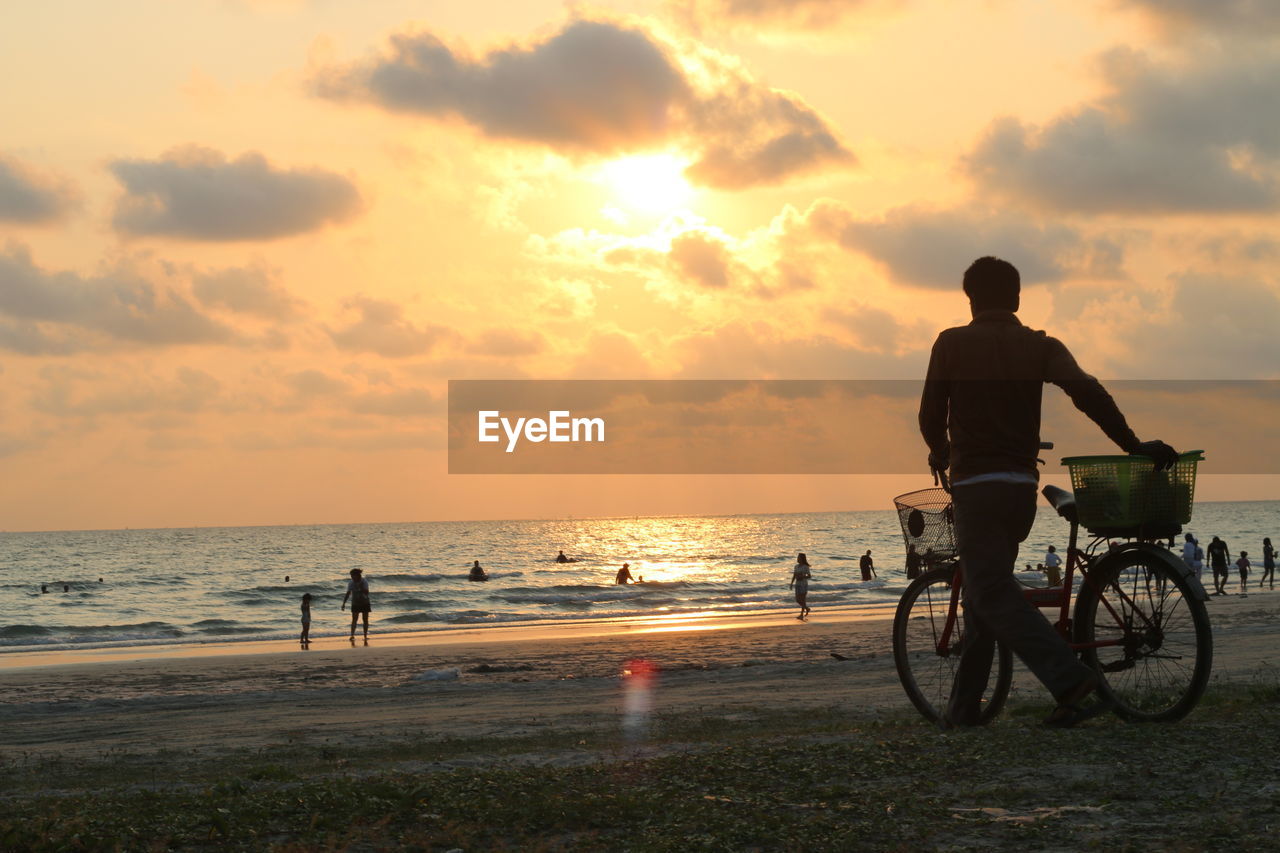 MAN RIDING BICYCLE ON BEACH AGAINST SKY
