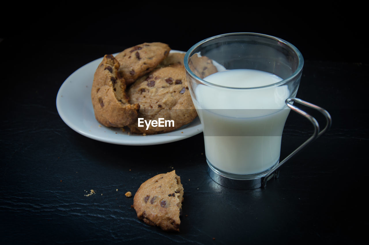Close-up of milk cup by cookies on table against black background