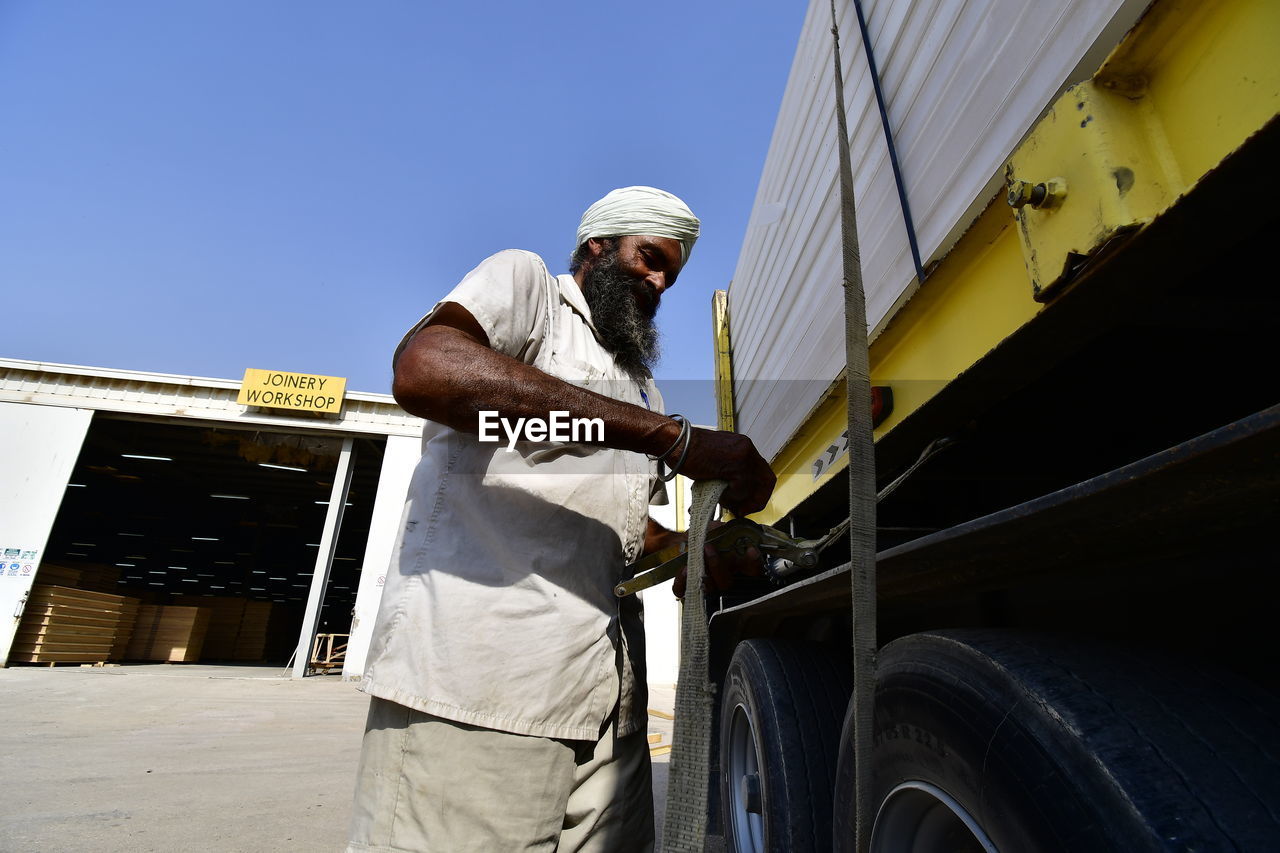 LOW ANGLE VIEW OF MAN WORKING AGAINST SKY