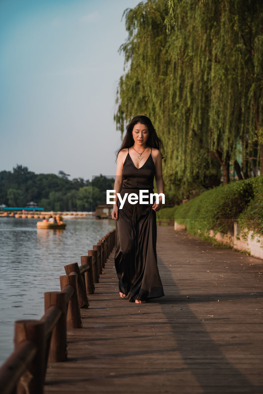 Full length portrait of woman standing on waterside against trees