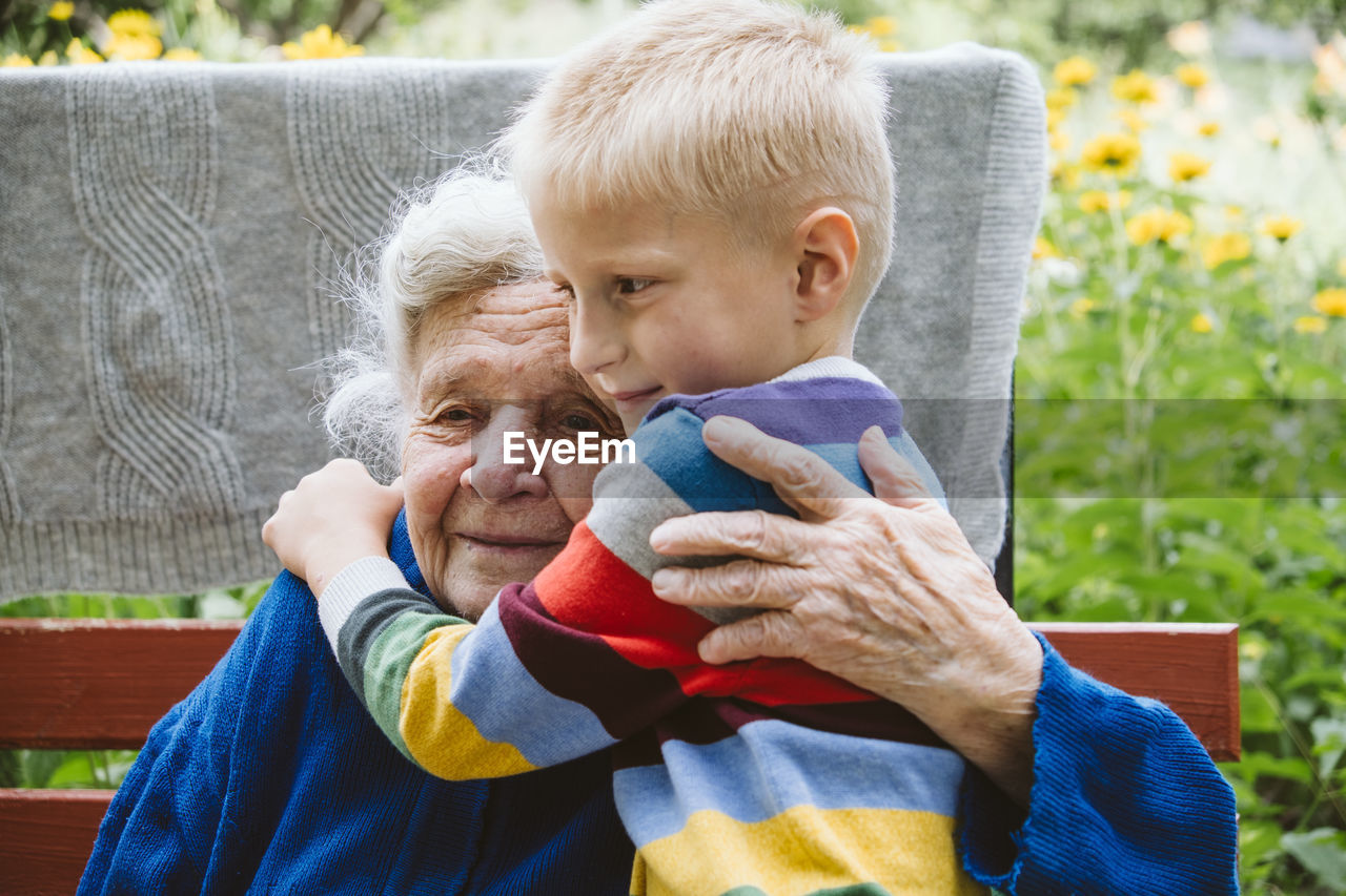 Grandmother embracing grandson while sitting on bench outdoors