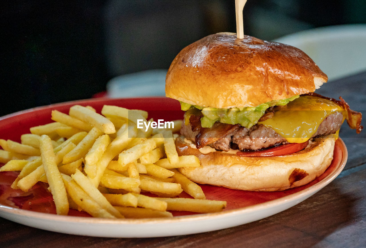 A close up image of a guacamole and bacon filled beef burger served with french fries