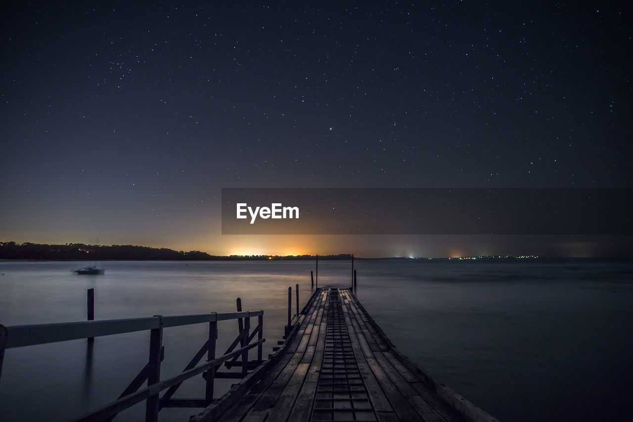 Pier over lake against sky at night