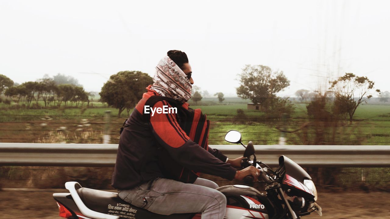 REAR VIEW OF MAN RIDING MOTORCYCLE ON ROAD