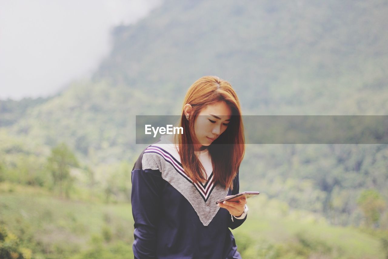 Young woman using mobile phone while standing on mountain