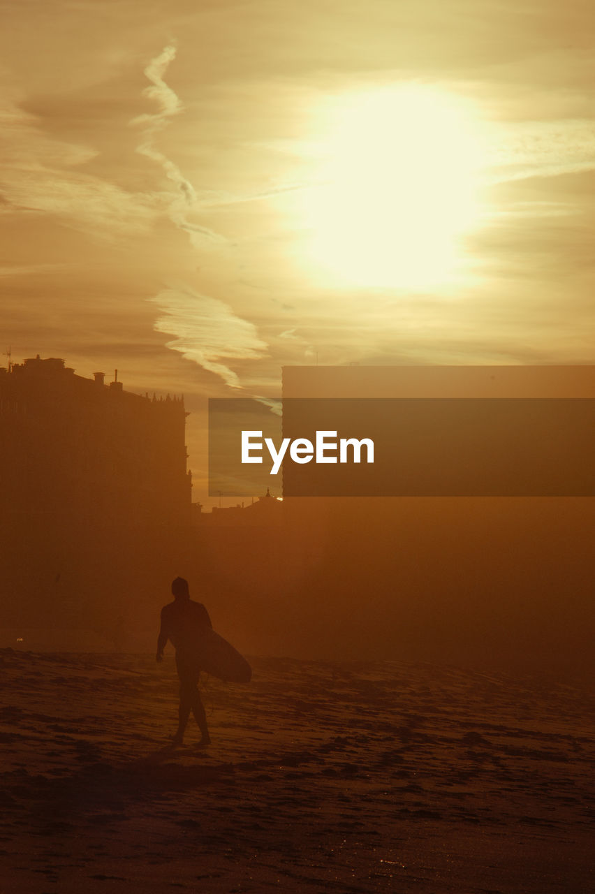 Silhouette of surfer walking on beach during sunset