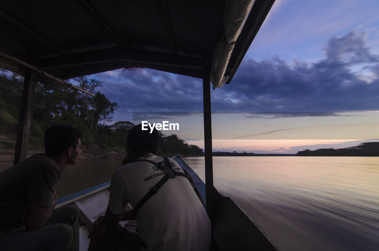Rear view of men traveling through boat in tambopata river against sky
