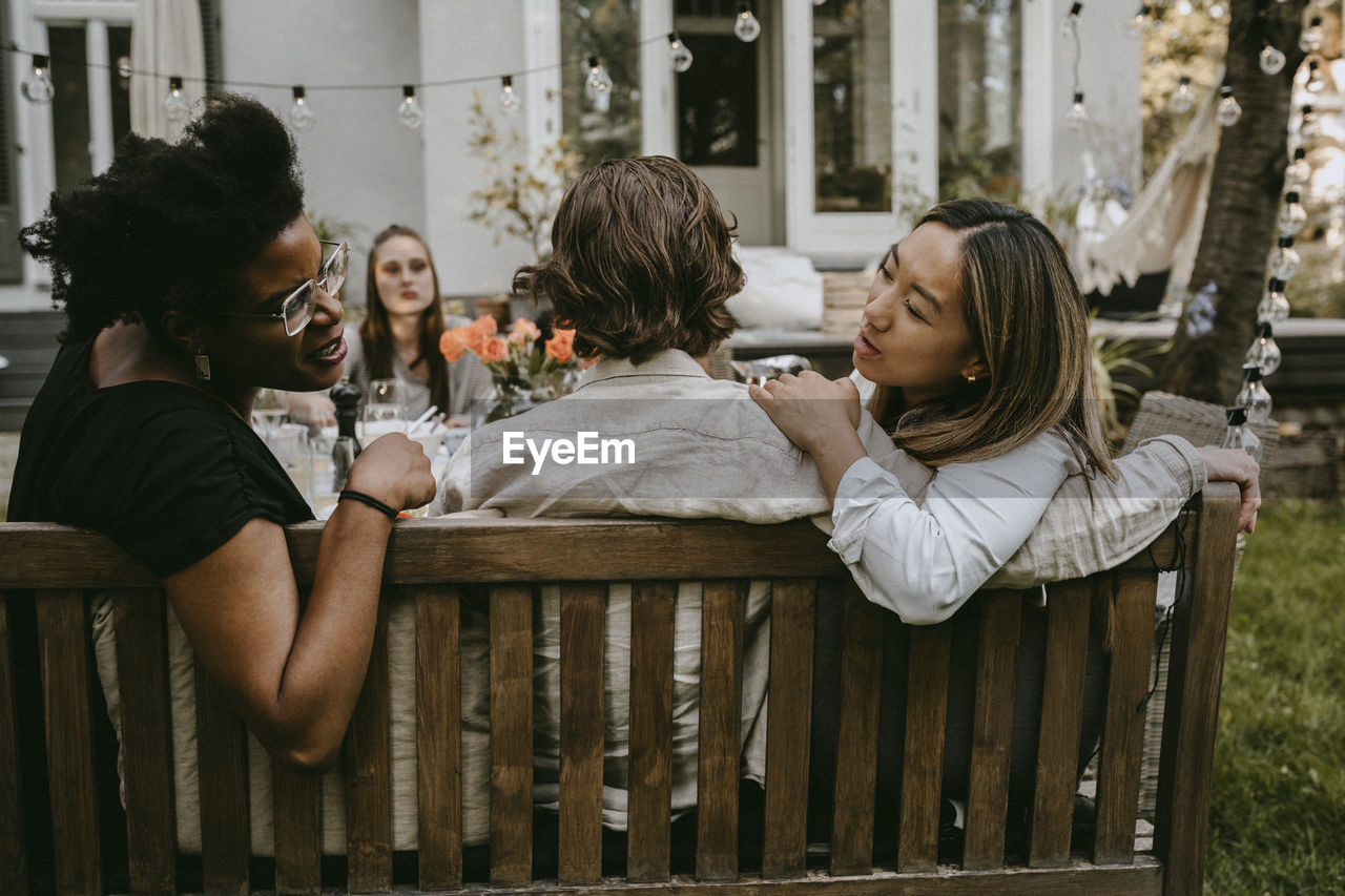 Female talking to young friend behind partner during social gathering