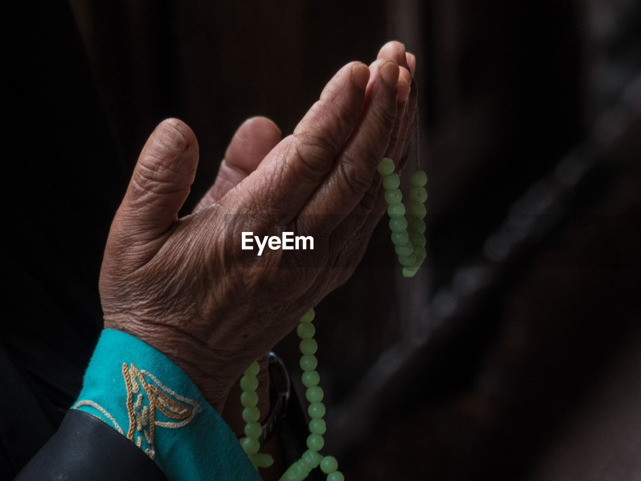 Cropped hand of woman with necklace praying in darkroom