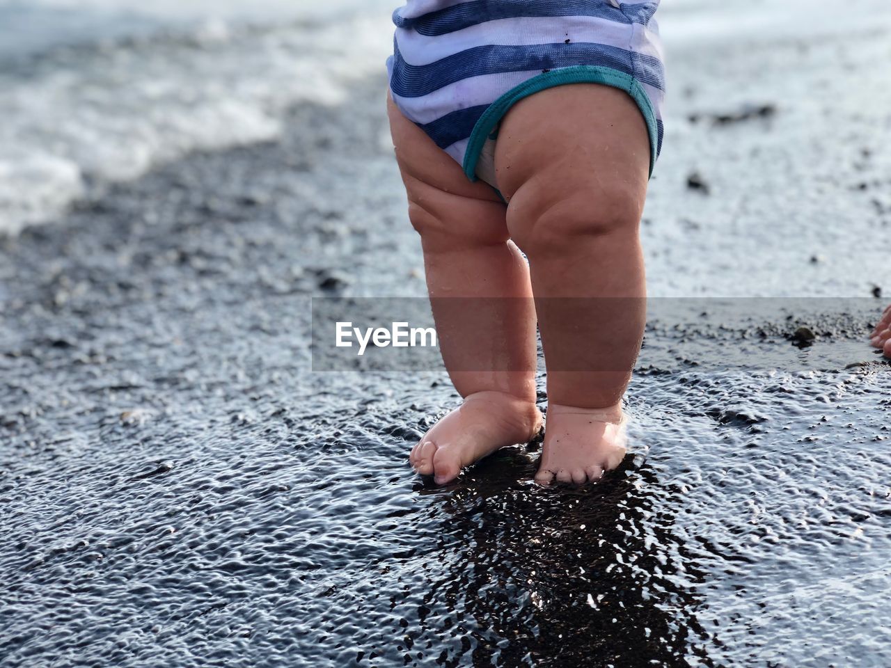 Low section of baby standing at beach