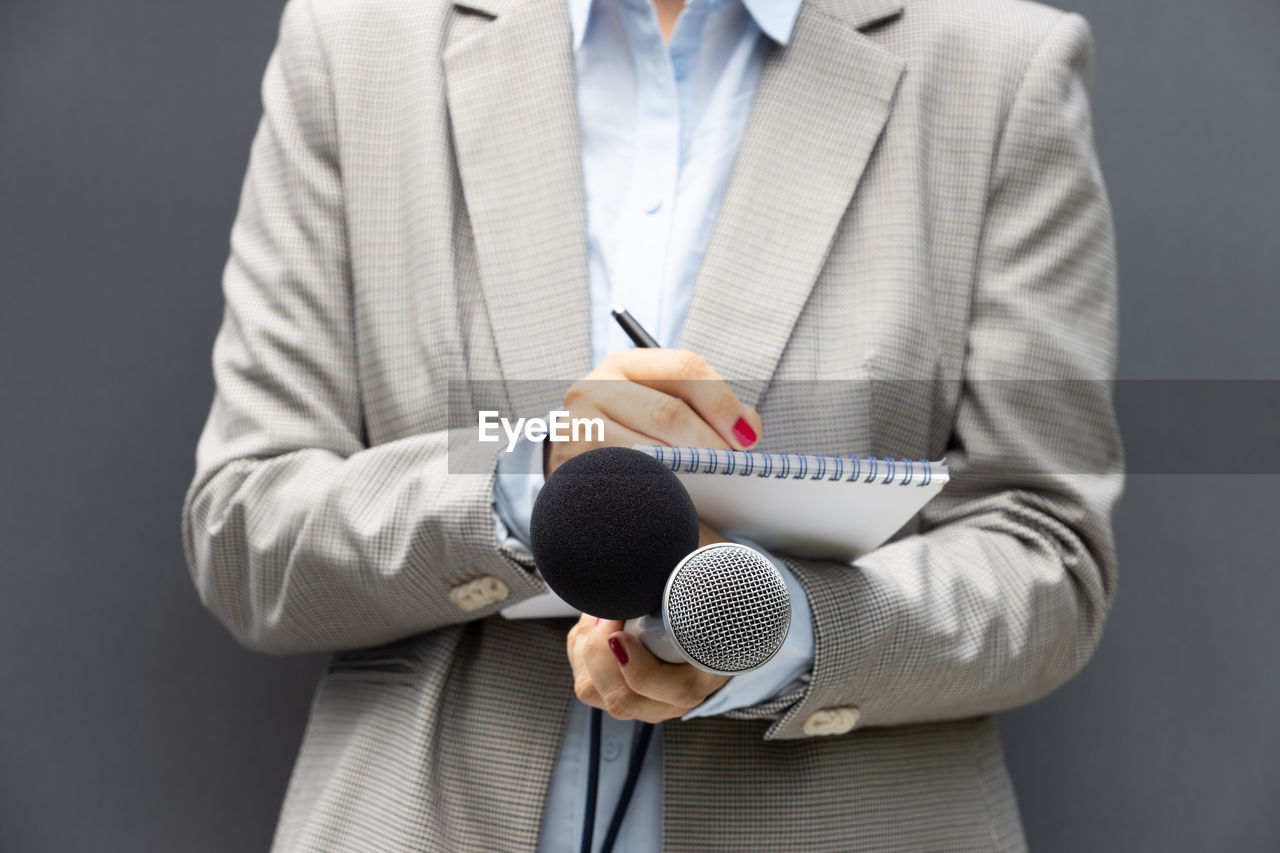 Female reporter at press conference or media event, writing notes, holding microphone