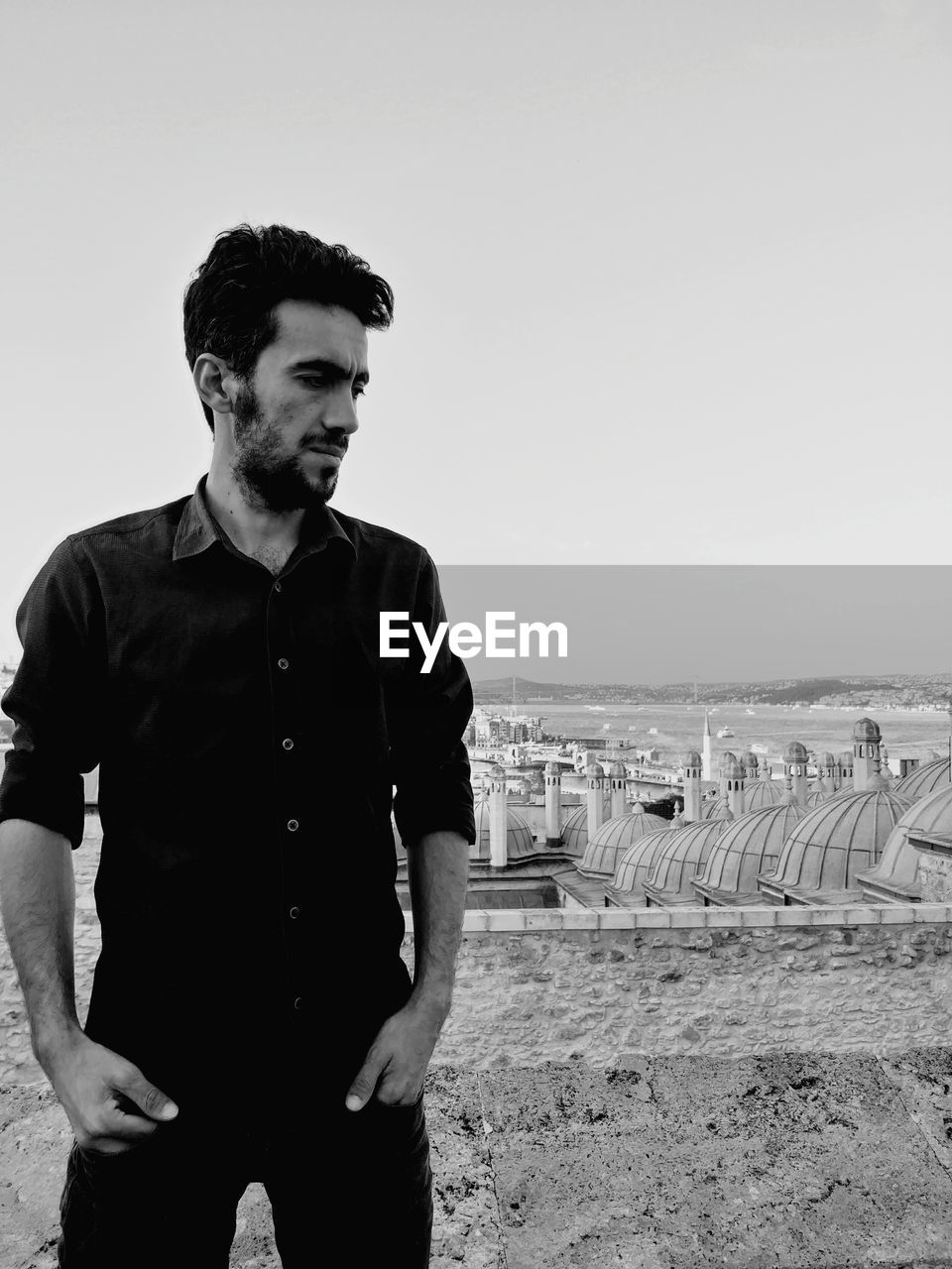 Young man standing on rooftop while looking away against clear sky