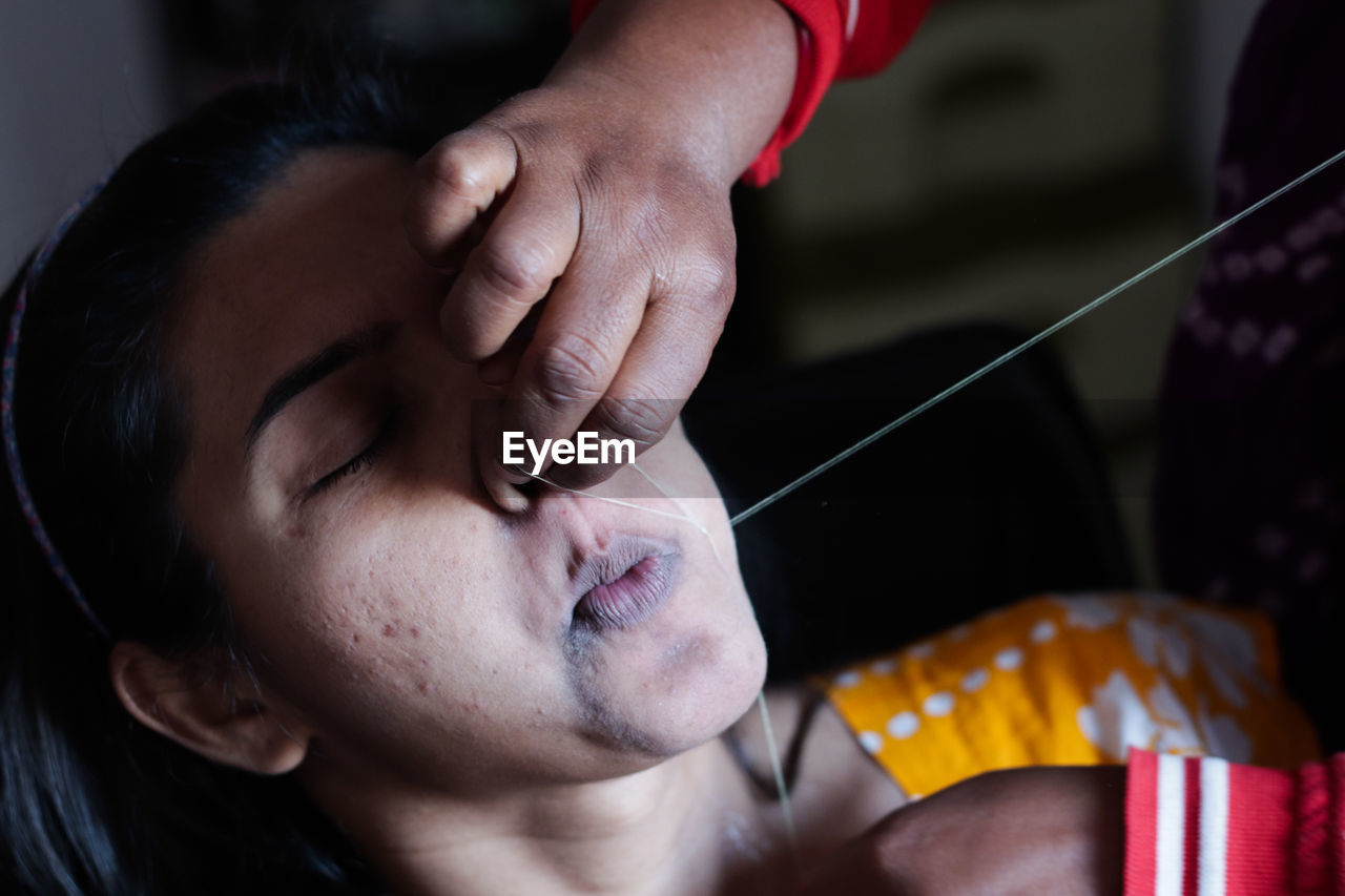 Cropped hands of beautician threading woman skin