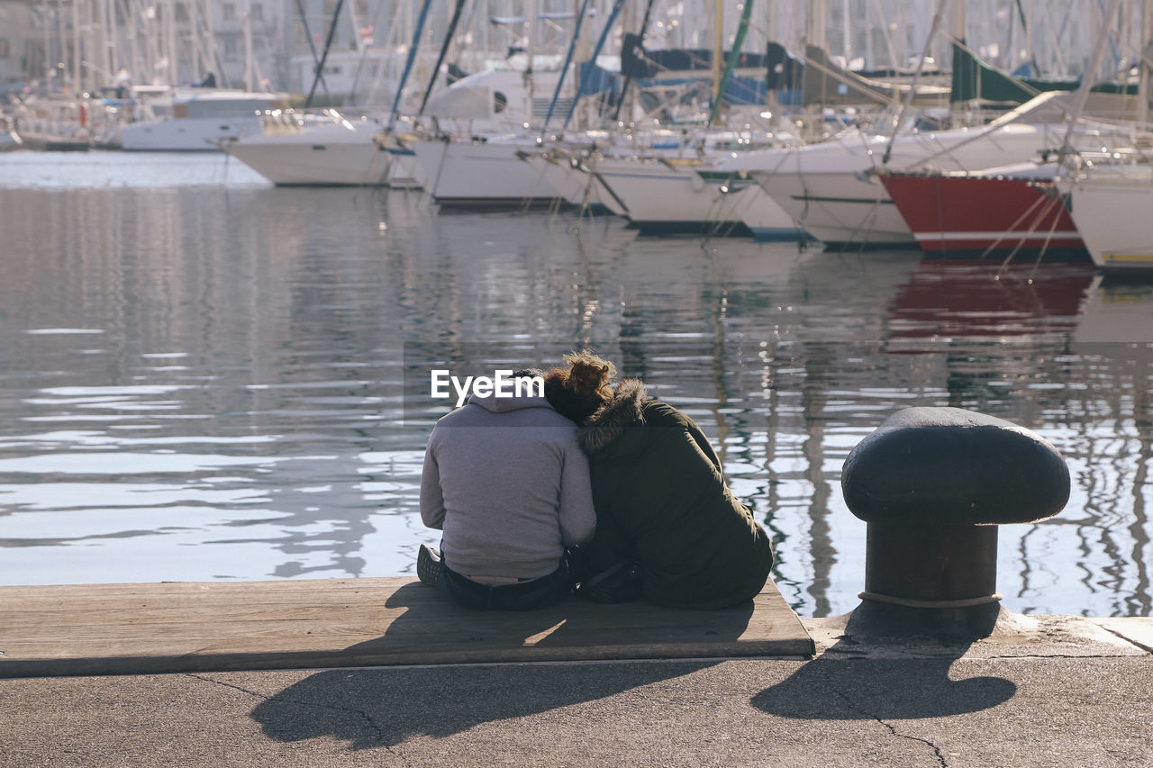 Rear view of couple sitting on pier over lake