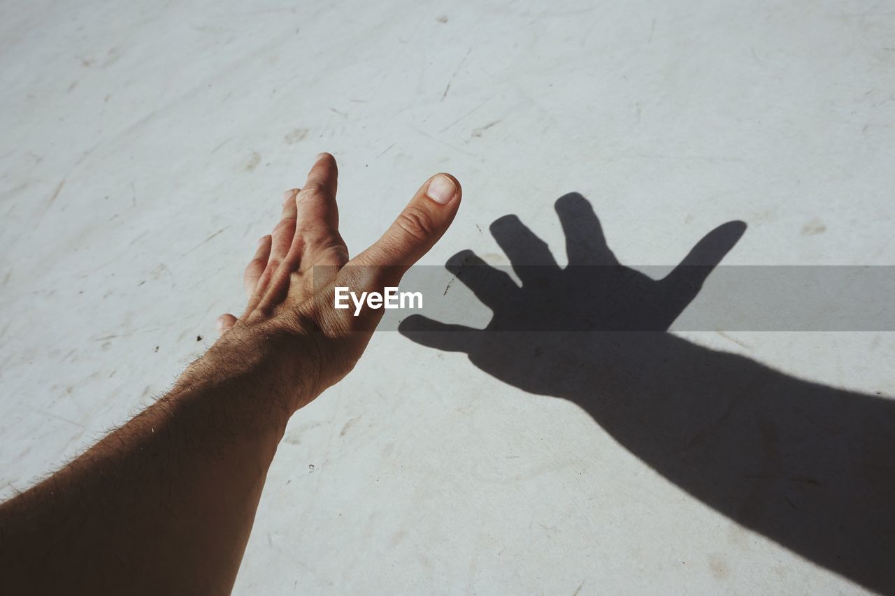 HIGH ANGLE VIEW OF PERSON SHADOW ON HAND AGAINST WALL