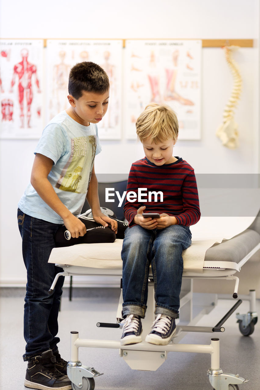 Brothers using smart phone at examination table in orthopedic clinic