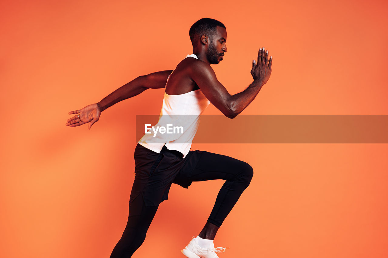 Side view of man running against orange background