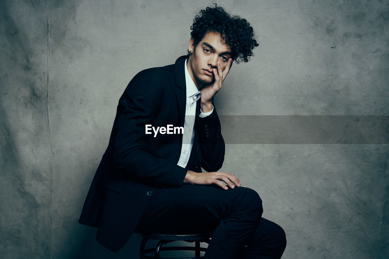 Young man sitting on chair against wall