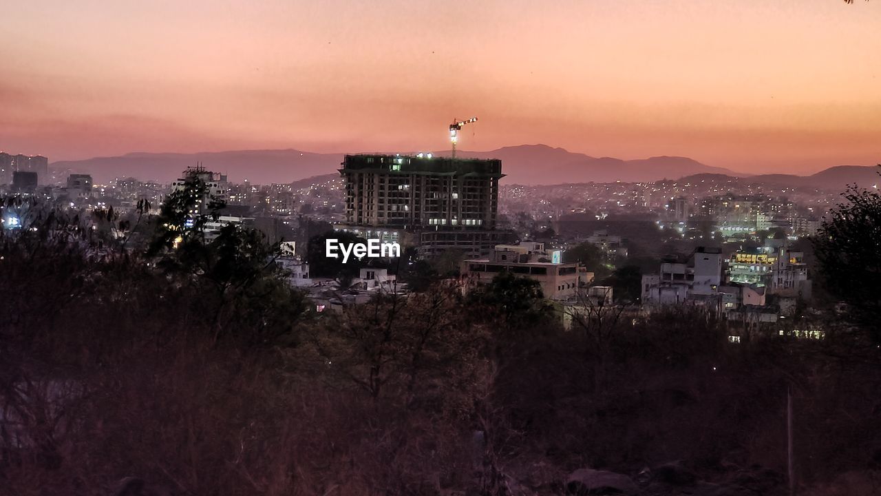 HIGH ANGLE VIEW OF ILLUMINATED BUILDINGS IN CITY AGAINST SKY