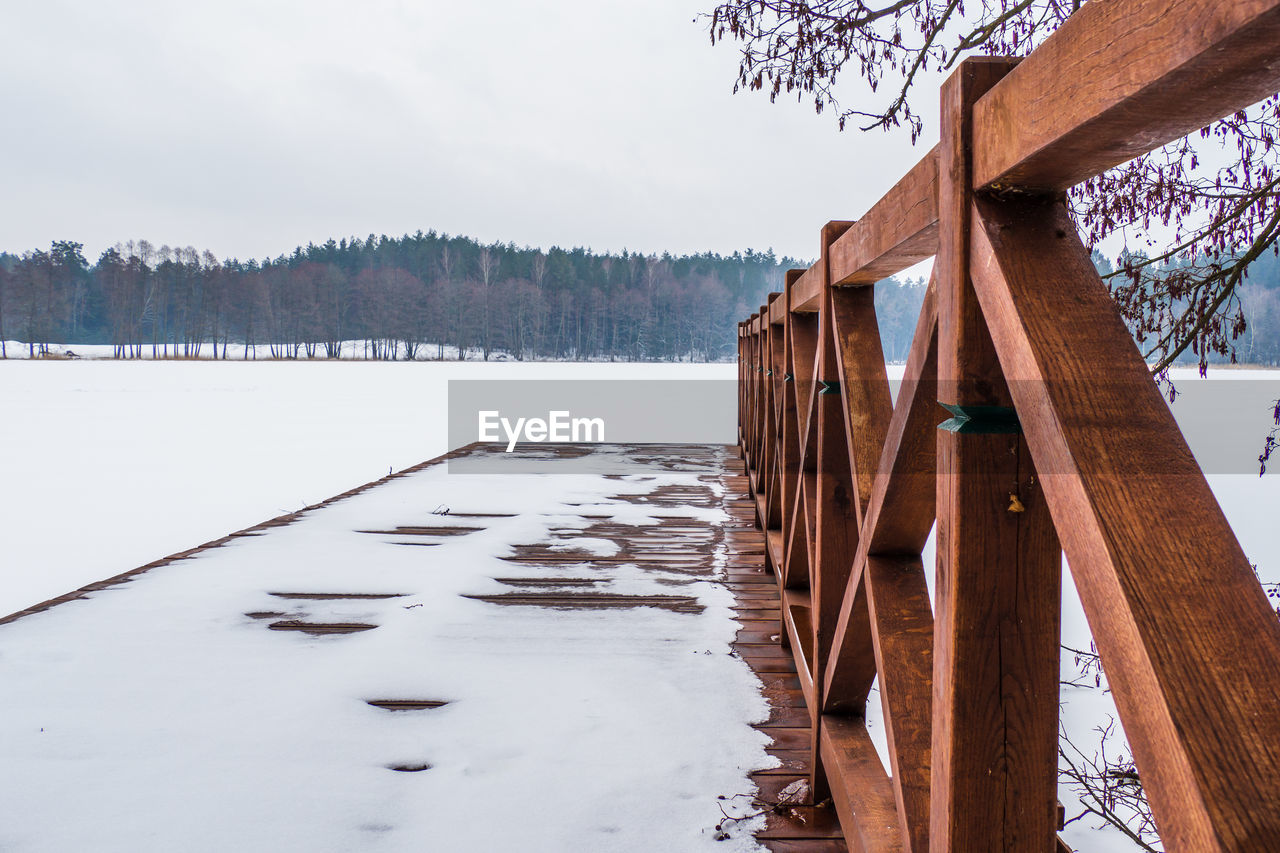 Winter landscape with wooden fishing bridge on frozen lake shore.