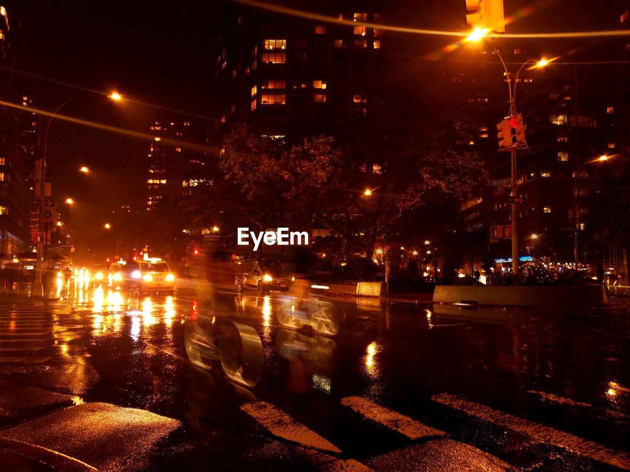 ILLUMINATED BUILDINGS BY WET STREET AT NIGHT