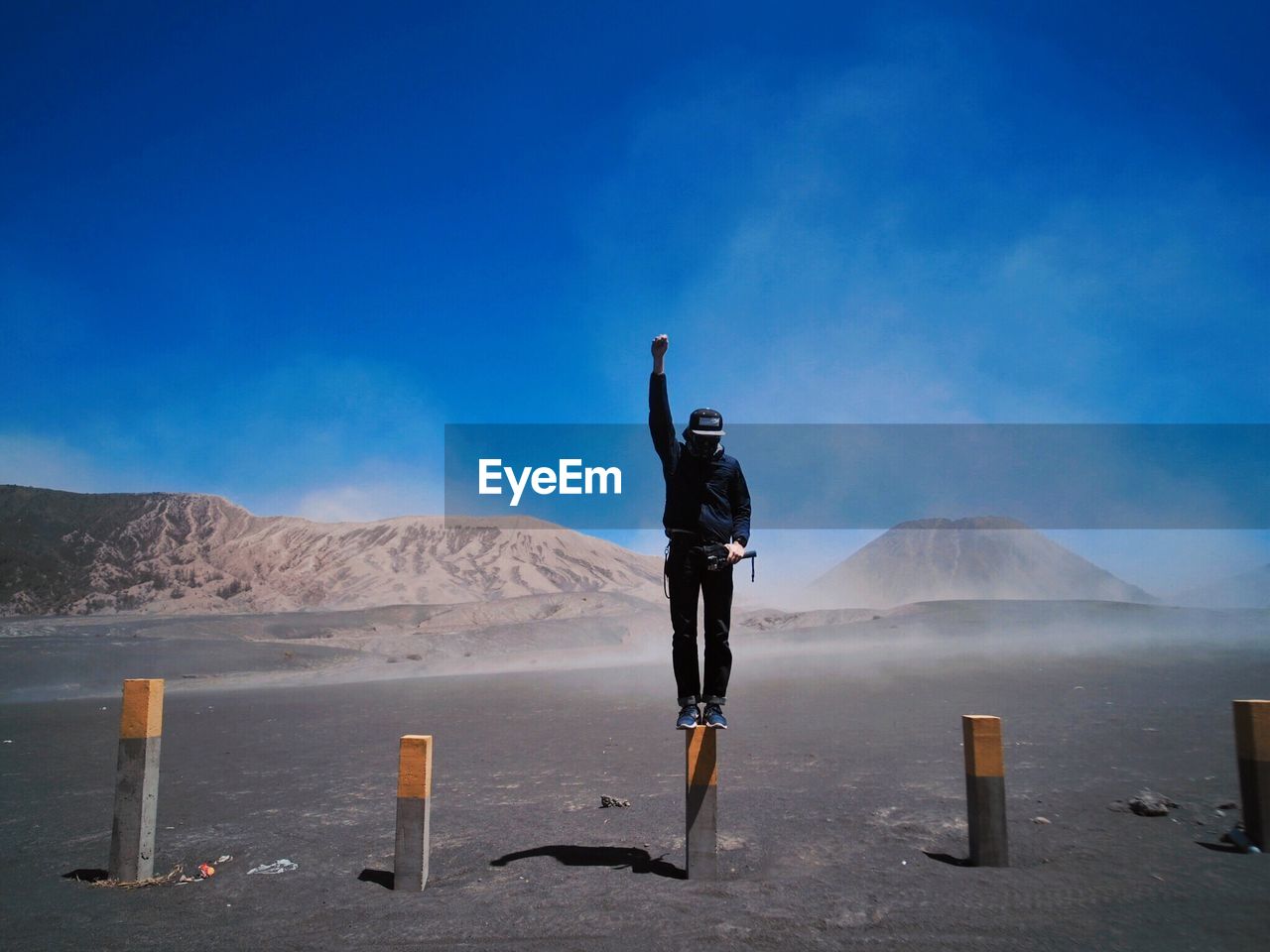 Full length of man standing on wooden post at desert against blue sky