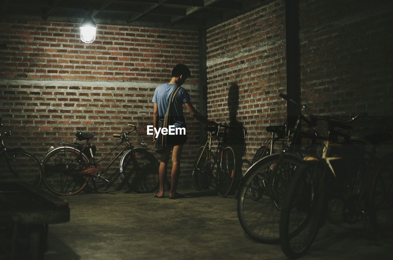 Rear view of man holding bicycle at illuminated parking lot