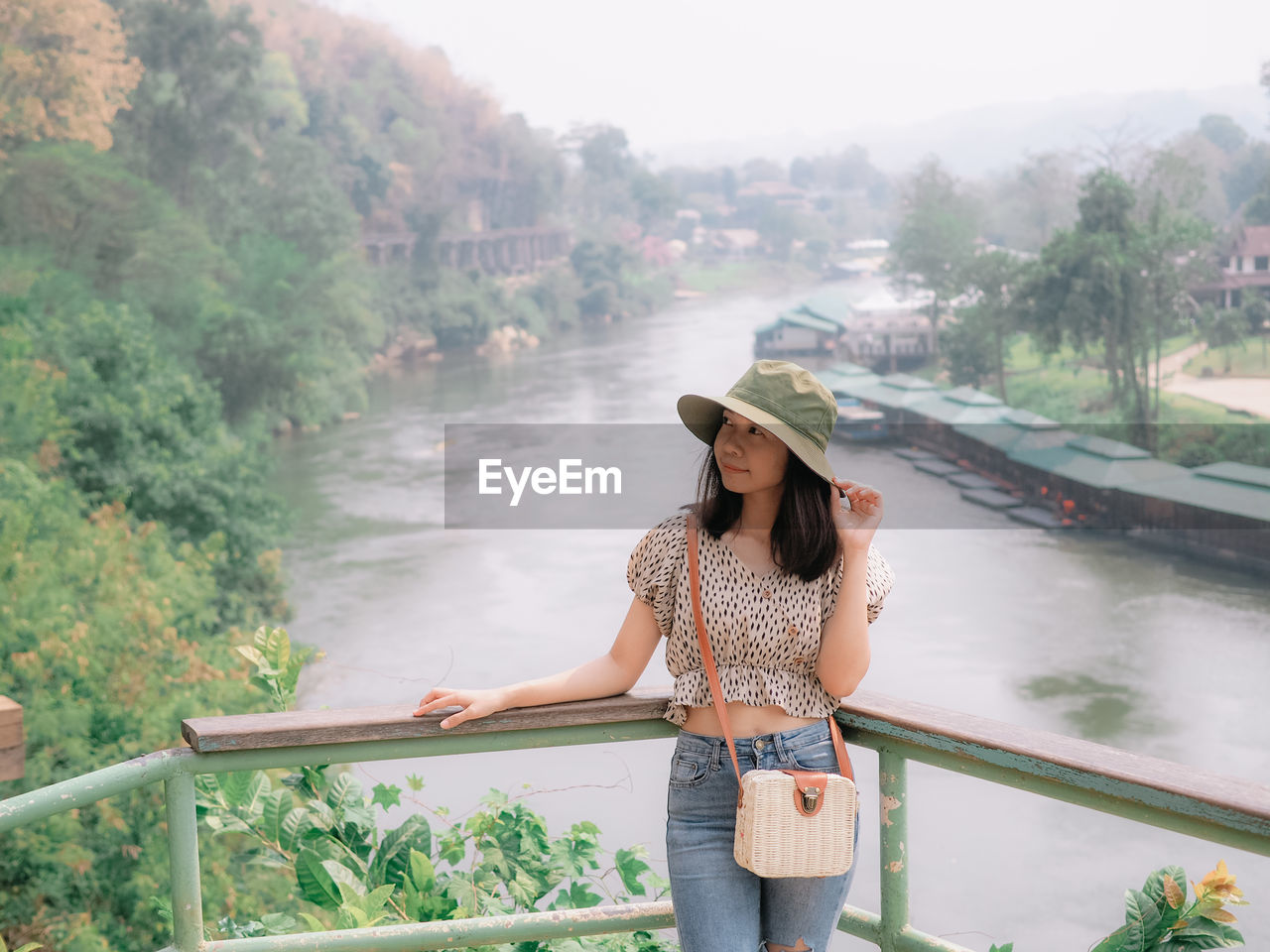 Young woman standing by railing against trees