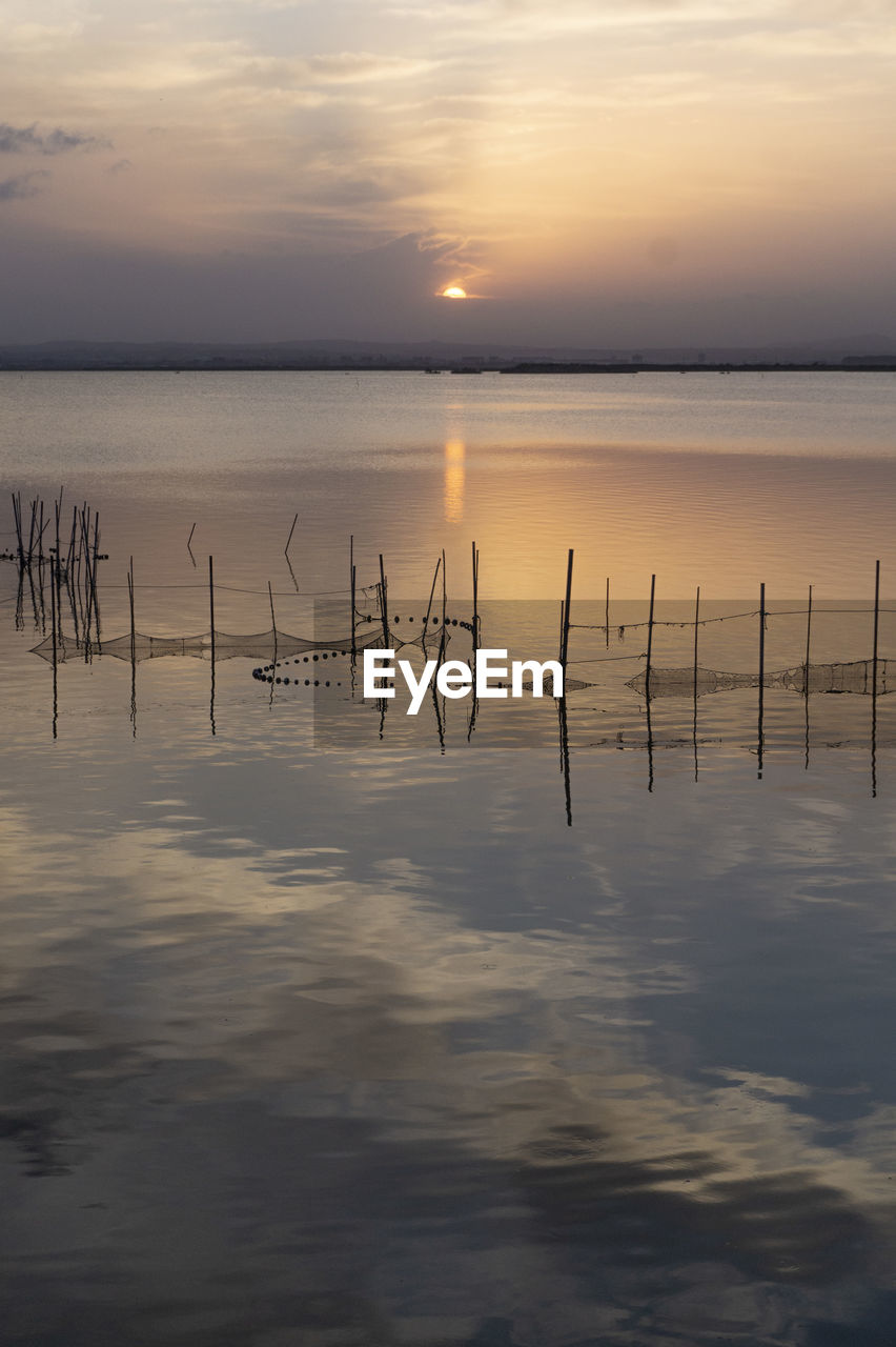 water, sky, reflection, sunset, beauty in nature, tranquility, scenics - nature, sea, tranquil scene, nature, horizon, dawn, shore, cloud, horizon over water, ocean, no people, evening, idyllic, environment, non-urban scene, wooden post, outdoors, beach, sun, wave, sunlight, landscape, wood, post, land, waterfront, seascape, silhouette, coast, dramatic sky