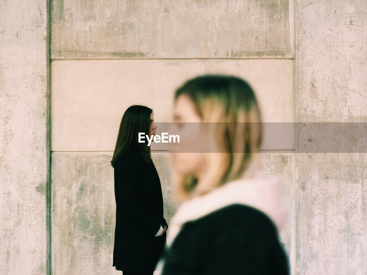 Side view of young women standing against wall