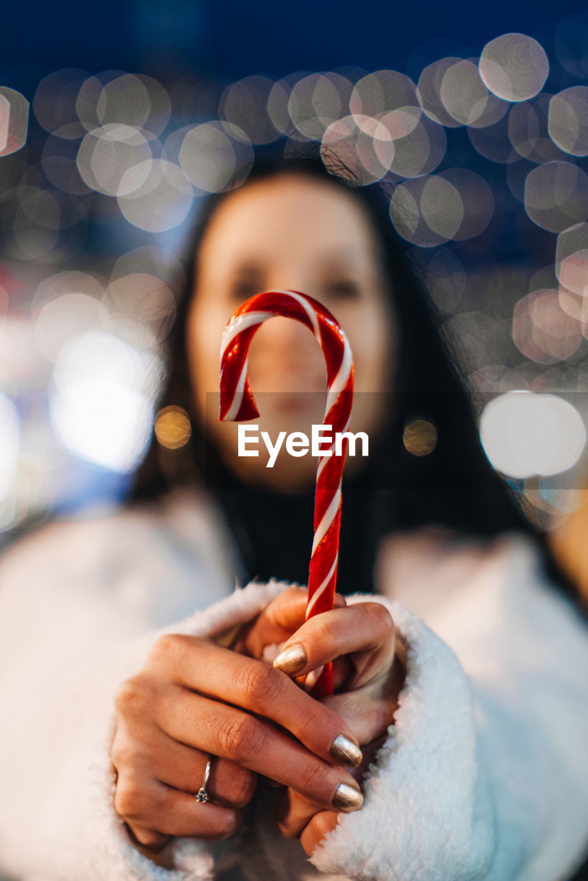 Female hand holding red white cane sweet lollipop. christmas holiday details