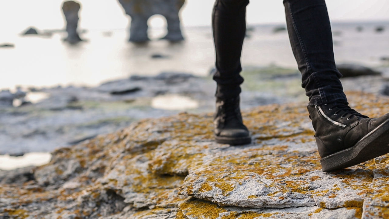 Low section of person walking on rock at beach