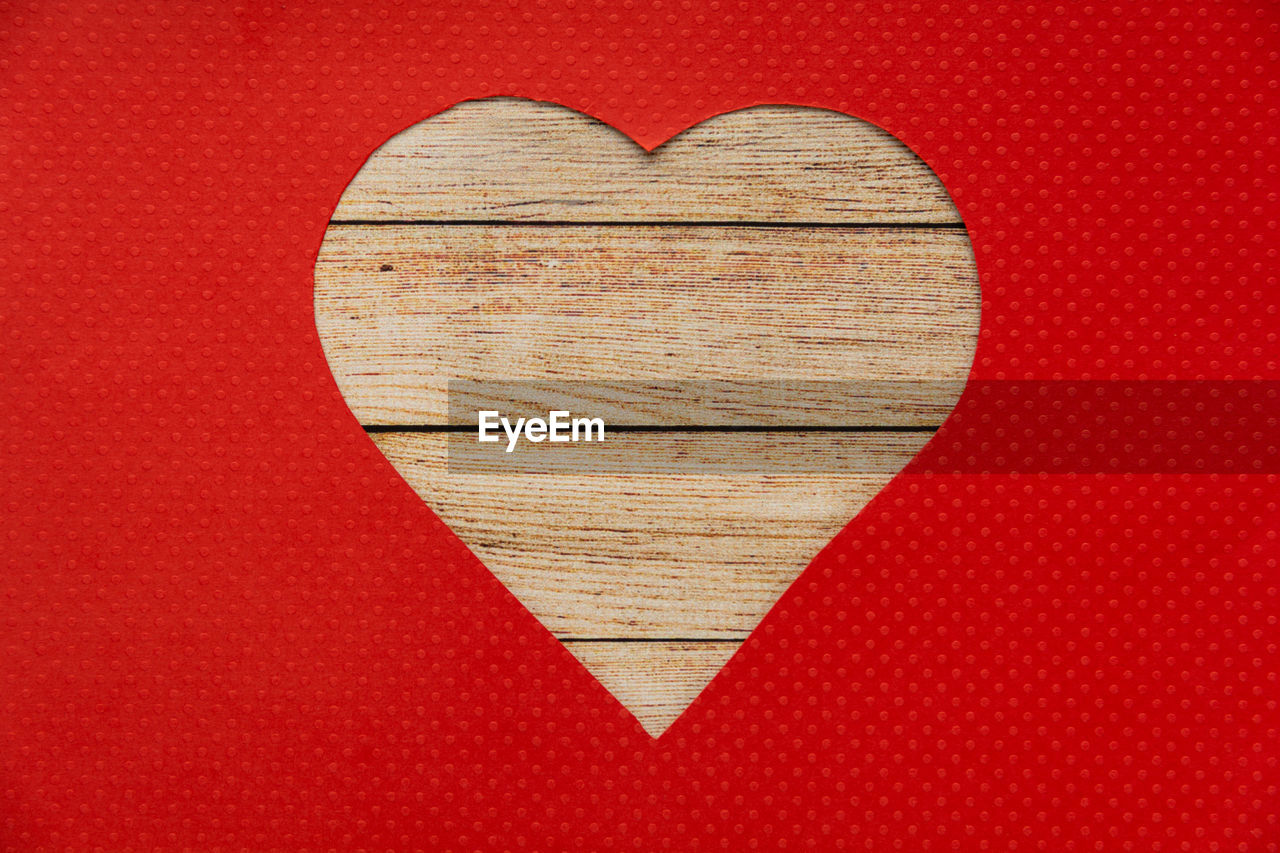 Heart shaped wooden hole torn through paper, isolated on red background. top view. 