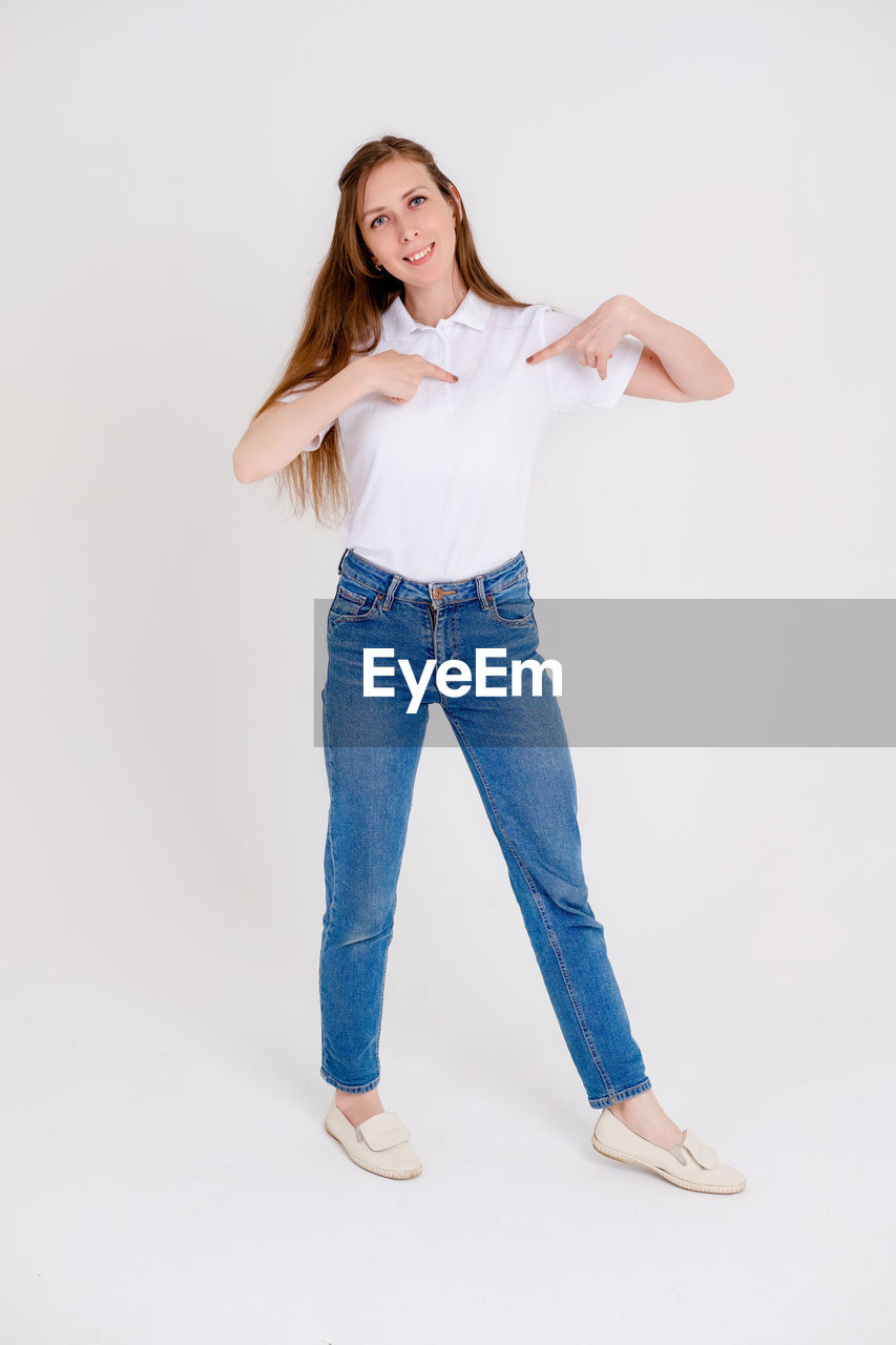 one person, studio shot, full length, portrait, women, smiling, indoors, casual clothing, white background, adult, young adult, looking at camera, jeans, happiness, long hair, emotion, photo shoot, clothing, hairstyle, denim, standing, front view, cut out, cheerful, positive emotion, teeth, female, smile, fashion, brown hair, trousers, copy space, limb, human leg, looking, person, arm