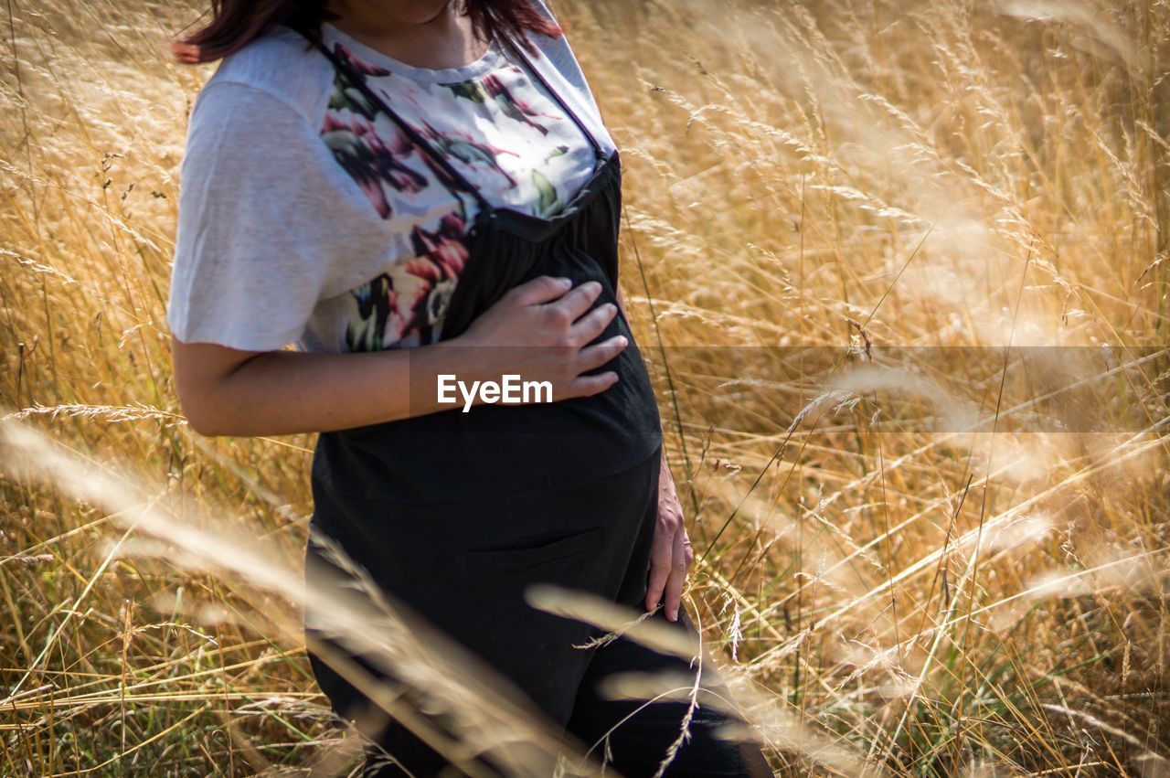 Midsection of pregnant woman standing on field