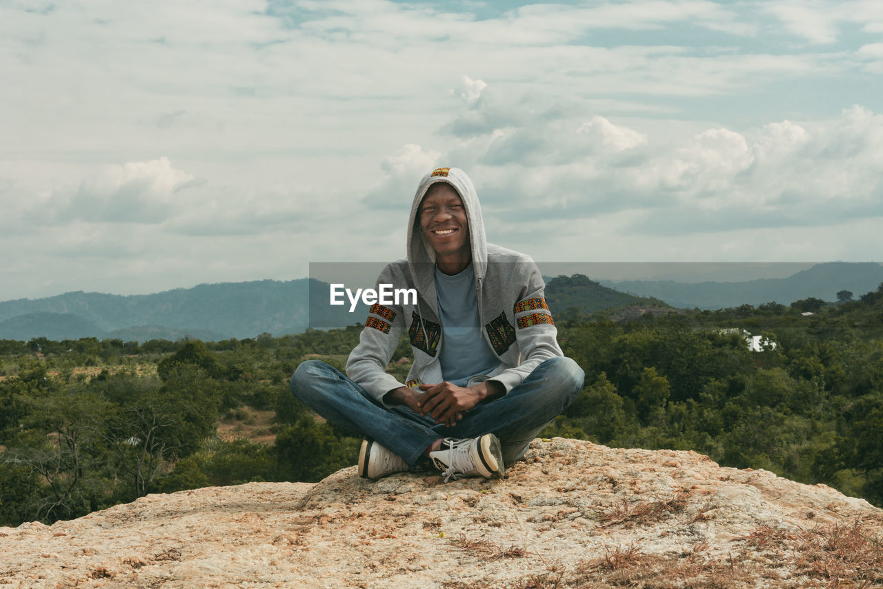 Full length of man sitting on mountain against sky