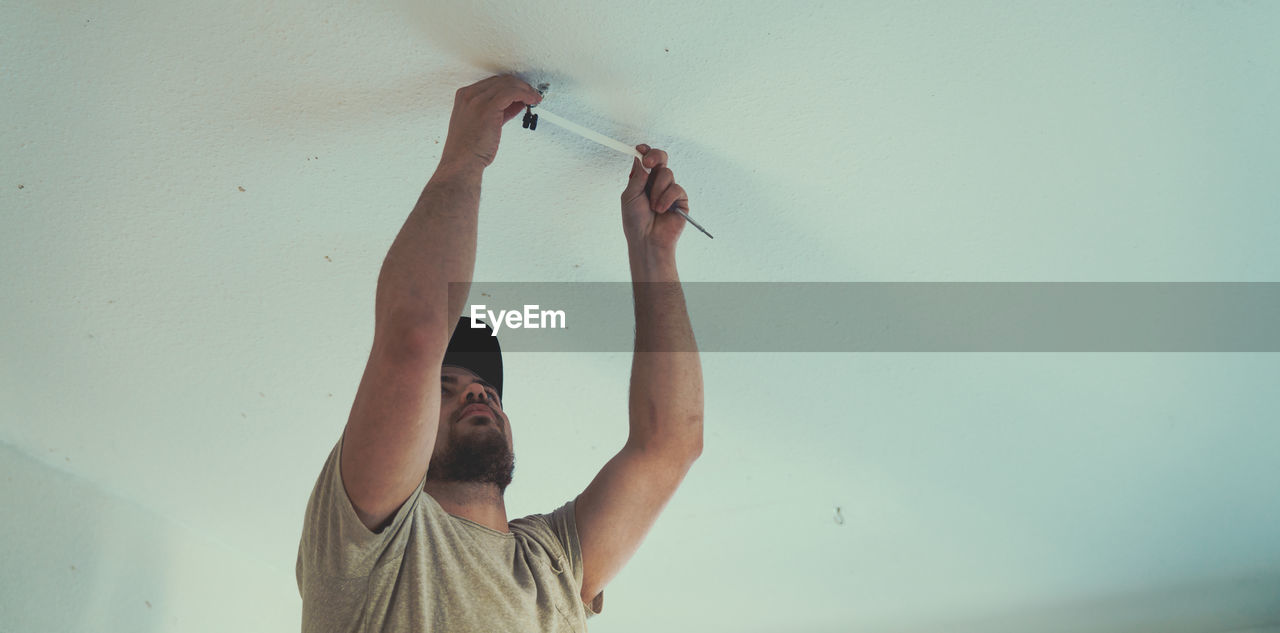 Low angle view of man repairing ceiling at home
