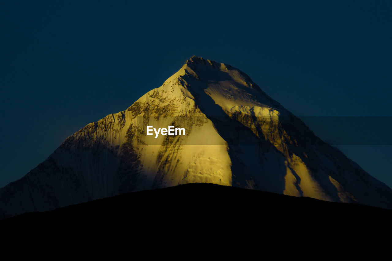 Low angle view of snowcapped mountain against clear blue sky