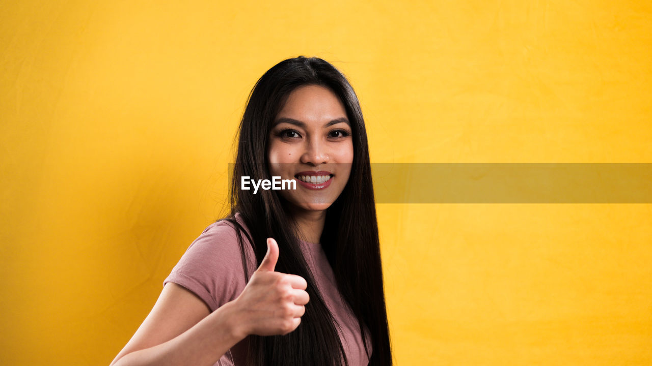 portrait, yellow, smiling, one person, women, adult, looking at camera, happiness, long hair, photo shoot, young adult, emotion, female, colored background, copy space, hairstyle, teenager, person, studio shot, yellow background, indoors, waist up, cheerful, teeth, portrait photography, wall - building feature, smile, lifestyles, standing, front view, positive emotion, human face, black hair, headshot, casual clothing, fashion
