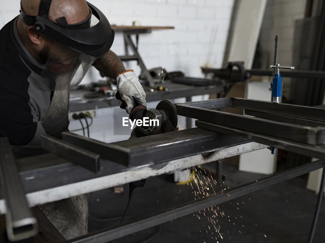 Side view of serious male welder using electric grinder and cutting metal detail in grungy workshop