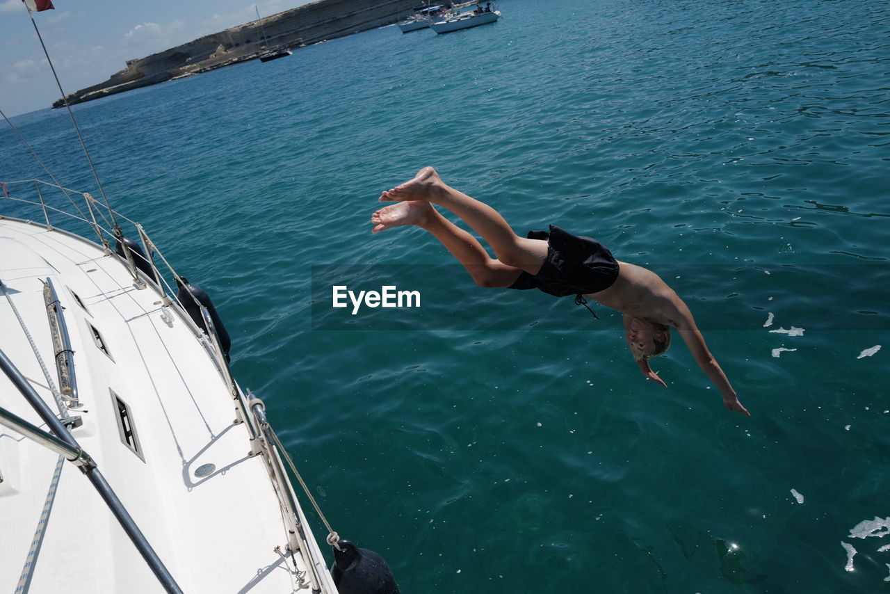 Shirtless man diving from boat into sea