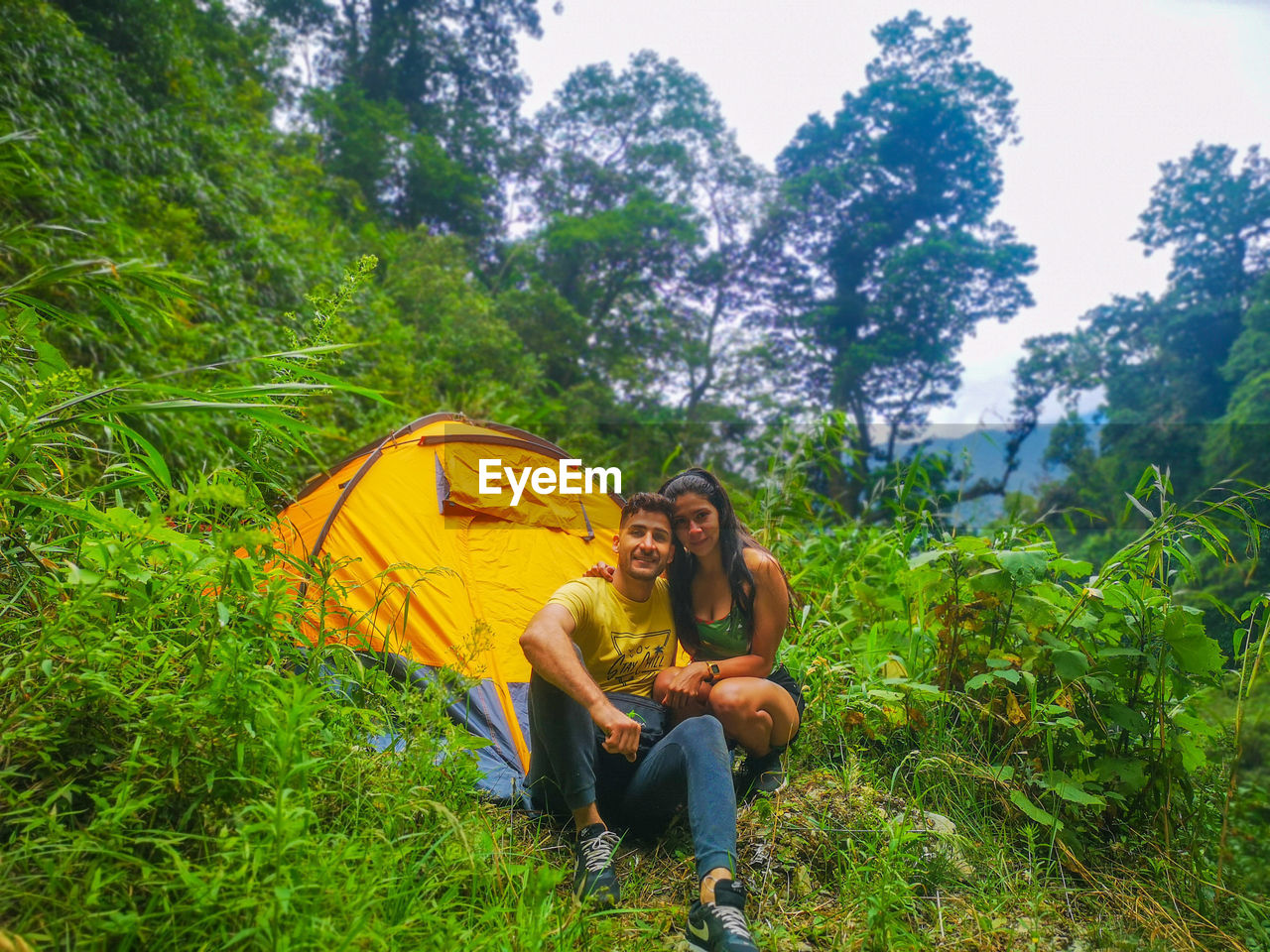 Young couple sitting on land against trees