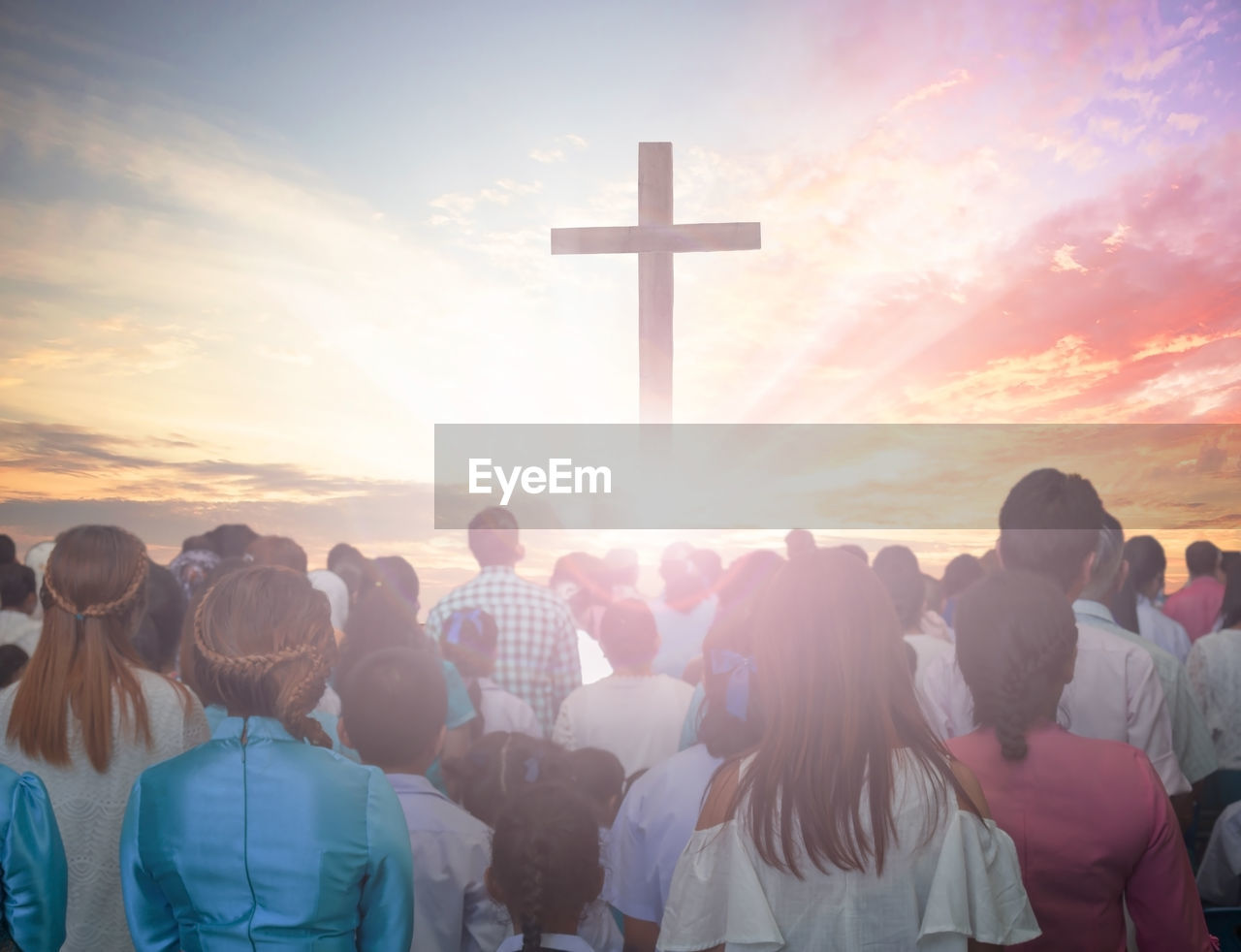 Digital composite image of crowd and cross against cloudy sky during sunset