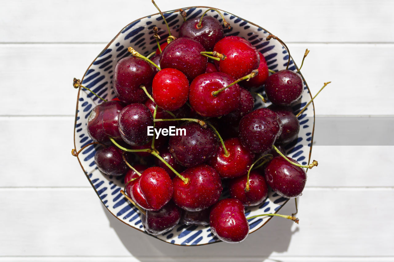 Top view of bowl with fresh and delicious cherries on white wooden table