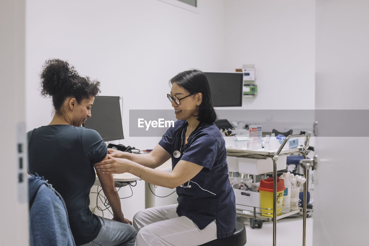 Smiling female doctor examining patient while discussing in medical clinic