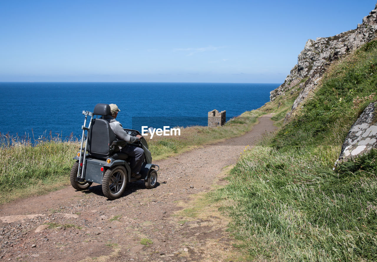 Man on vehicle on dirt road by sea