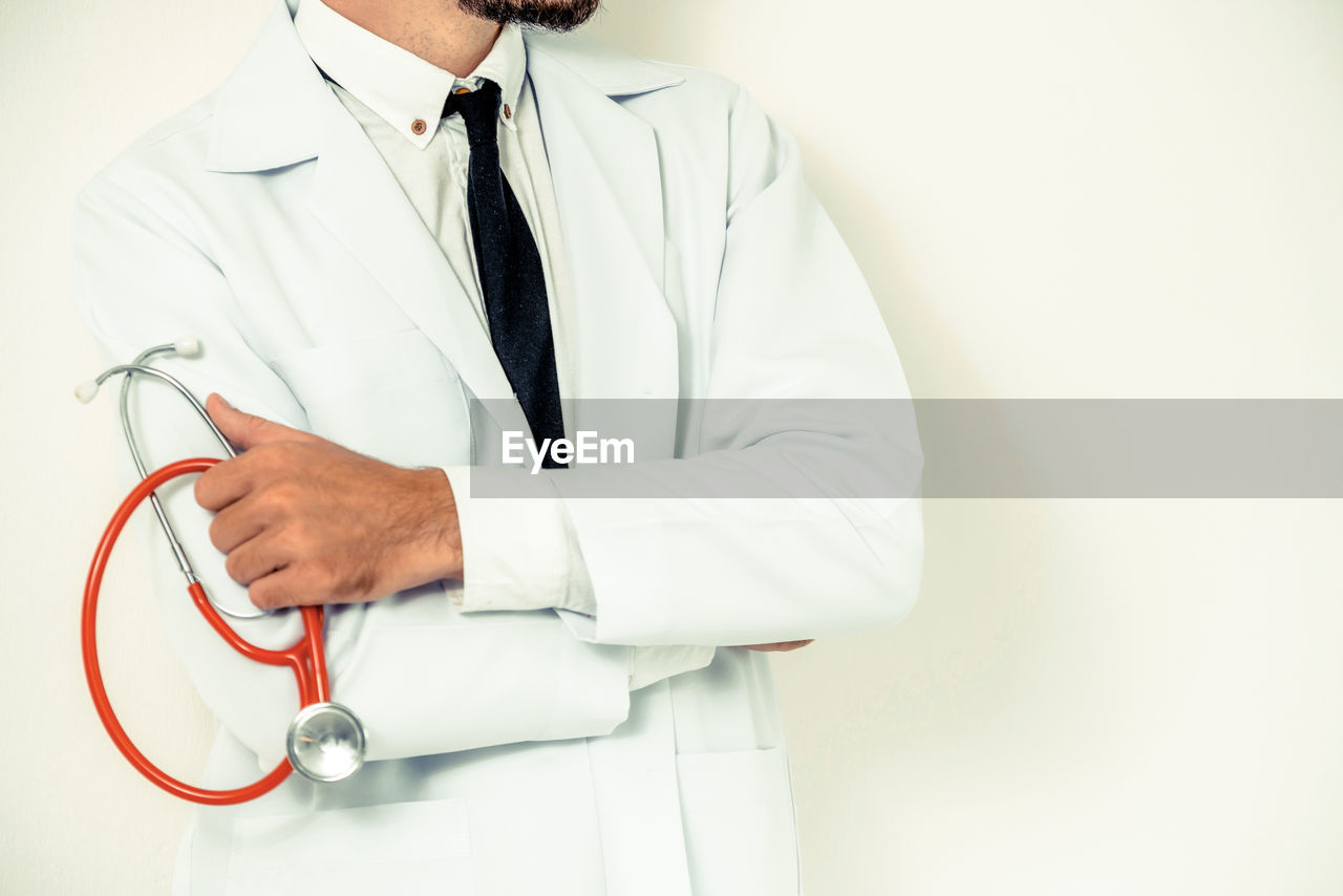 Midsection of doctor showing thumbs up while standing on white background