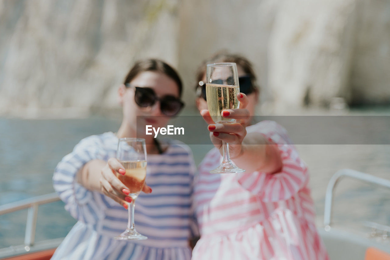 Portrait of caucasian beautiful girls in sunglasses sitting in a boat holding glasses of champagne