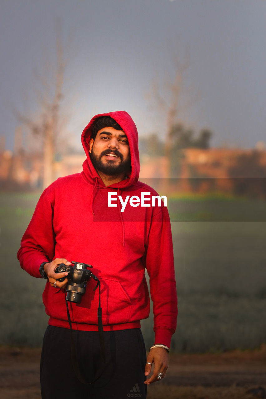 Portrait of young man holding camera while standing outdoors